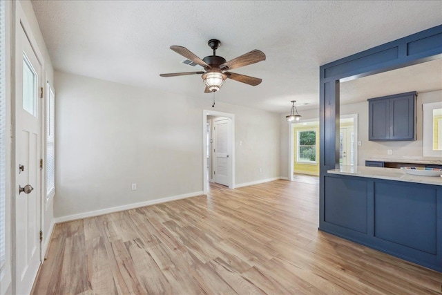 unfurnished living room with light wood-style floors, ceiling fan, baseboards, and a textured ceiling