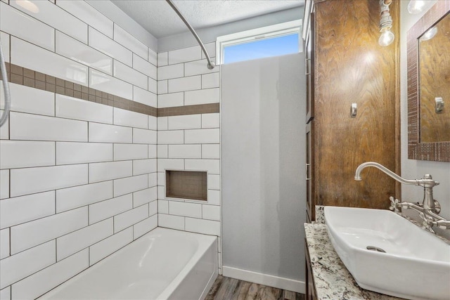 bathroom with a sink, wood finished floors, baseboards, tub / shower combination, and a textured ceiling