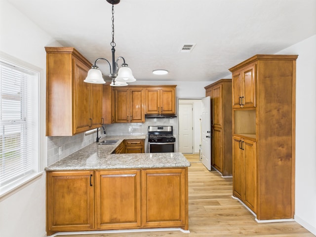 1832 19th St, Port Arthur, TX 77640 - kitchen with stainless steel gas stove, a peninsula, a chandelier, light wood-style flooring, and under cabinet range hood
