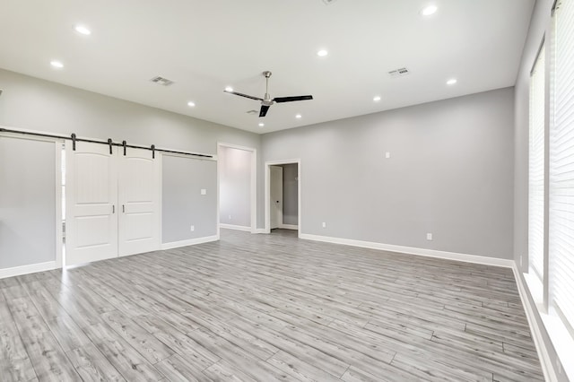 unfurnished bedroom with light wood-type flooring, a barn door, and ceiling fan