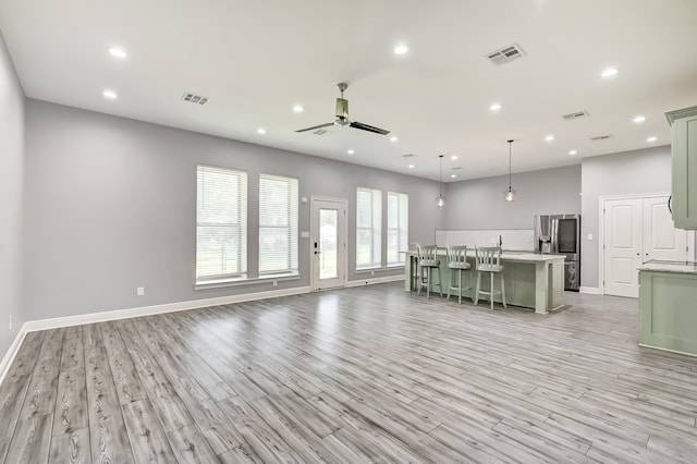 kitchen featuring ceiling fan, a kitchen breakfast bar, stainless steel fridge with ice dispenser, pendant lighting, and a center island with sink