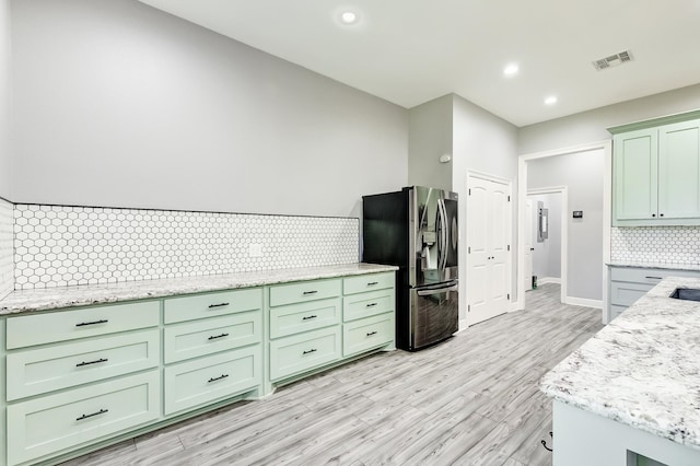 kitchen with light stone counters, stainless steel fridge with ice dispenser, backsplash, and light wood-type flooring