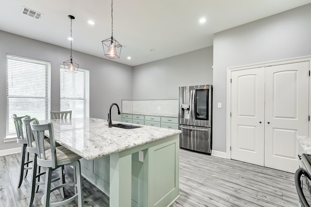 kitchen featuring stainless steel fridge, green cabinets, sink, and a kitchen island with sink