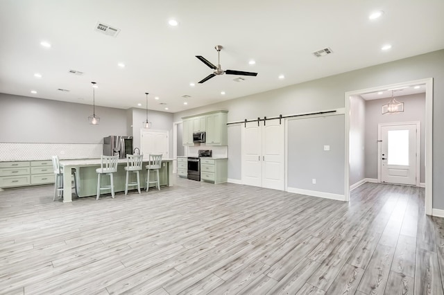 kitchen with pendant lighting, a barn door, light wood-type flooring, an island with sink, and stainless steel appliances