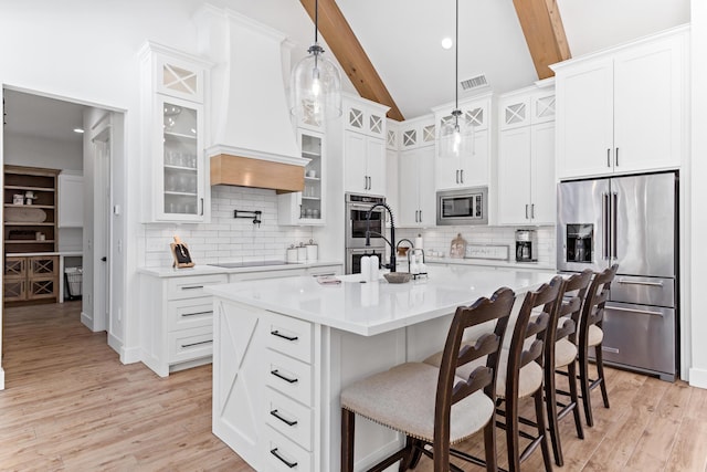 kitchen with pendant lighting, stainless steel appliances, white cabinetry, and a center island with sink