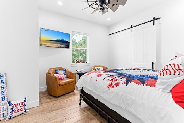 bedroom featuring ceiling fan, a barn door, and light wood-type flooring