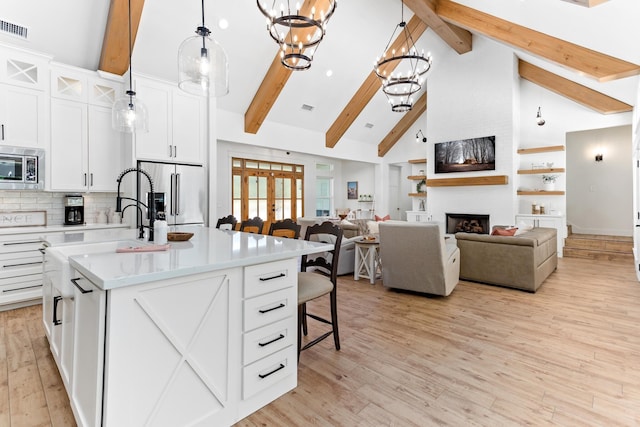 kitchen featuring hanging light fixtures, stainless steel appliances, a fireplace, white cabinets, and a center island with sink