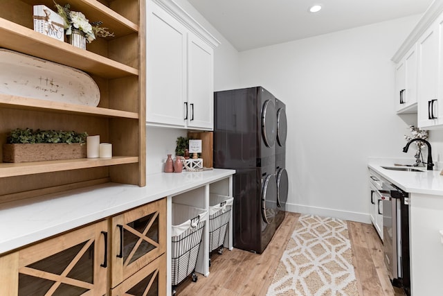 laundry area with light hardwood / wood-style floors, cabinets, stacked washing maching and dryer, and sink