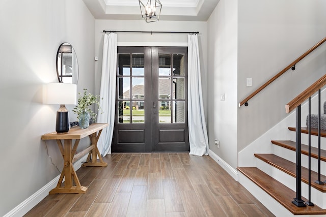 entryway featuring hardwood / wood-style floors, a notable chandelier, a raised ceiling, crown molding, and french doors