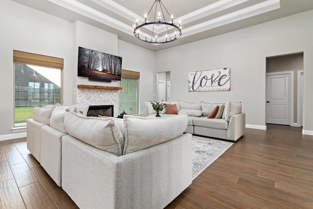 living room featuring dark hardwood / wood-style floors, a chandelier, a tiled fireplace, a high ceiling, and a raised ceiling