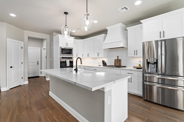 kitchen featuring an island with sink, white cabinetry, sink, custom exhaust hood, and stainless steel appliances