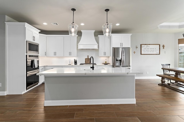 kitchen with white cabinetry, a center island with sink, custom exhaust hood, and appliances with stainless steel finishes