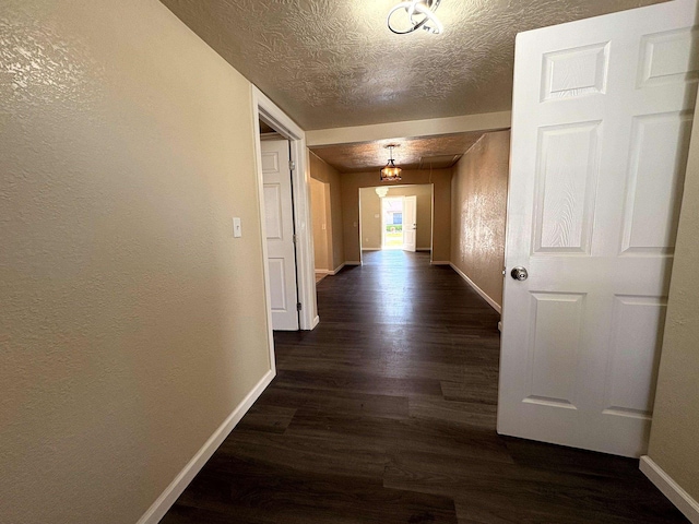 hall with a textured ceiling, dark wood-type flooring, baseboards, and a textured wall