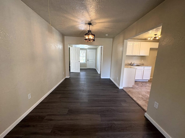 hallway featuring a sink, baseboards, a textured ceiling, and dark wood-style flooring