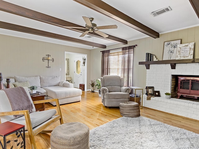 living room featuring beam ceiling, a wood stove, ceiling fan, and hardwood / wood-style flooring