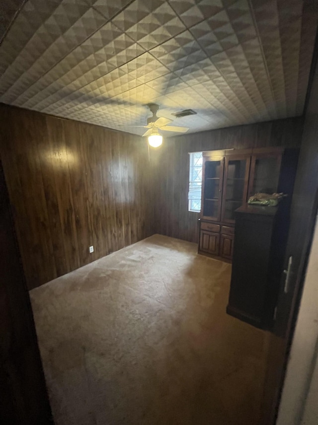 carpeted empty room featuring ceiling fan and wood walls