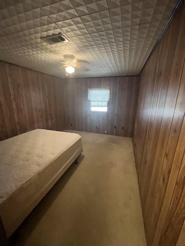 unfurnished bedroom with ceiling fan, wooden walls, and carpet