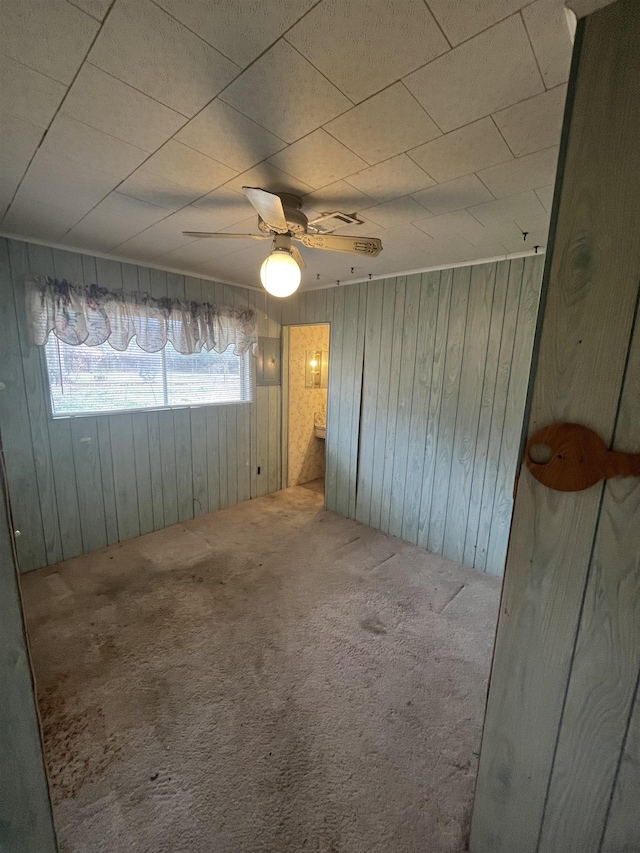 spare room featuring ceiling fan, carpet, and wood walls