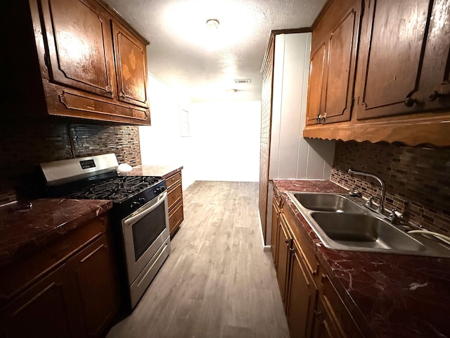 5335 Landry Ln, Beaumont, TX 77708 - kitchen featuring stainless steel range with gas cooktop, a sink, tasteful backsplash, light wood finished floors, and dark countertops