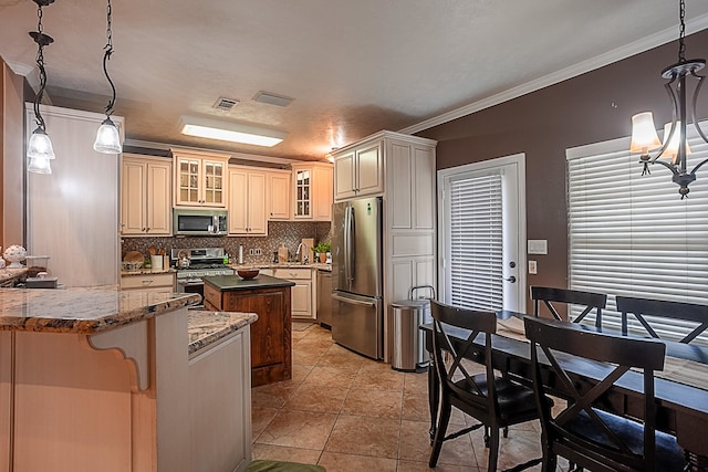 kitchen featuring appliances with stainless steel finishes, dark stone countertops, hanging light fixtures, ornamental molding, and cream cabinetry