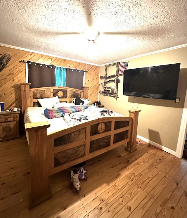 bedroom with crown molding, wooden walls, wood-type flooring, and a textured ceiling