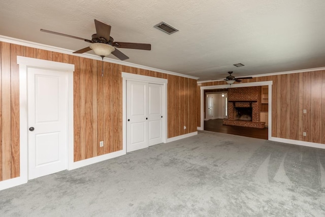 unfurnished living room with carpet, a fireplace, visible vents, a ceiling fan, and crown molding