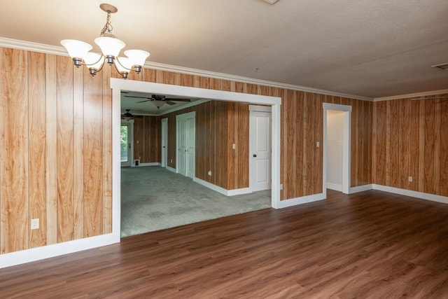 empty room featuring ornamental molding, wooden walls, and ceiling fan with notable chandelier