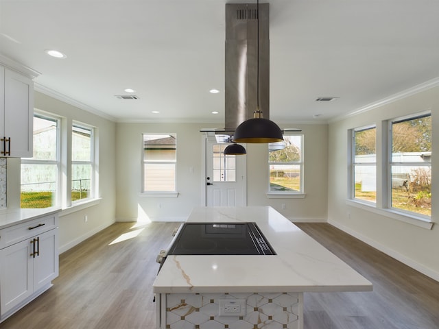 kitchen with light stone counters, white cabinetry, crown molding, and a center island