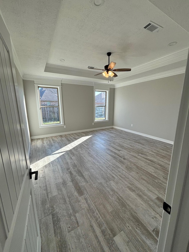 empty room with ceiling fan, a raised ceiling, ornamental molding, a textured ceiling, and light wood-type flooring