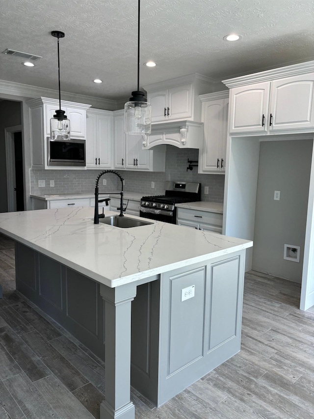 kitchen with light stone counters, stainless steel appliances, a center island with sink, white cabinets, and hanging light fixtures