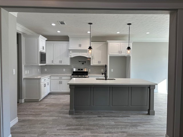 kitchen with gas range, white cabinetry, light hardwood / wood-style flooring, an island with sink, and pendant lighting