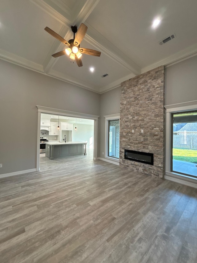 unfurnished living room featuring ceiling fan, beam ceiling, a stone fireplace, and wood-type flooring