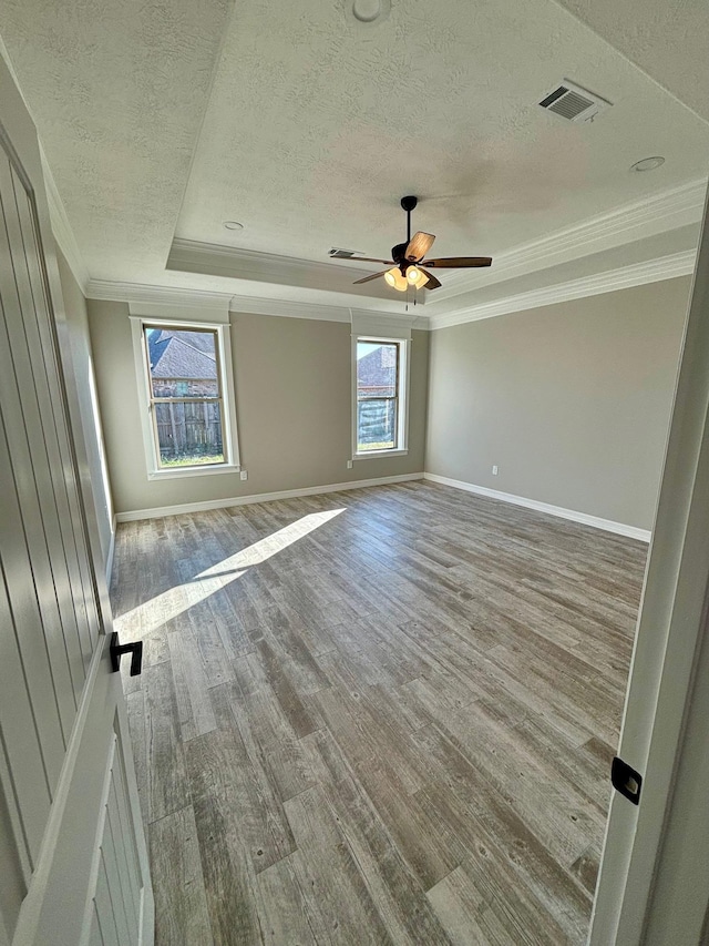 empty room with ceiling fan, a raised ceiling, light hardwood / wood-style flooring, a textured ceiling, and ornamental molding