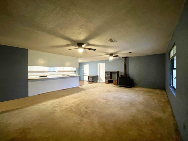 unfurnished living room with ceiling fan, a wood stove, and a textured ceiling