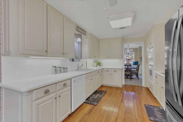 kitchen featuring sink, backsplash, a chandelier, white appliances, and light wood-type flooring