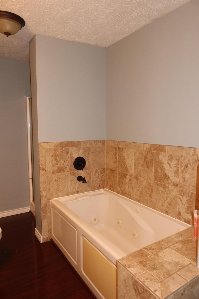 bathroom with a textured ceiling, wood-type flooring, and a bath