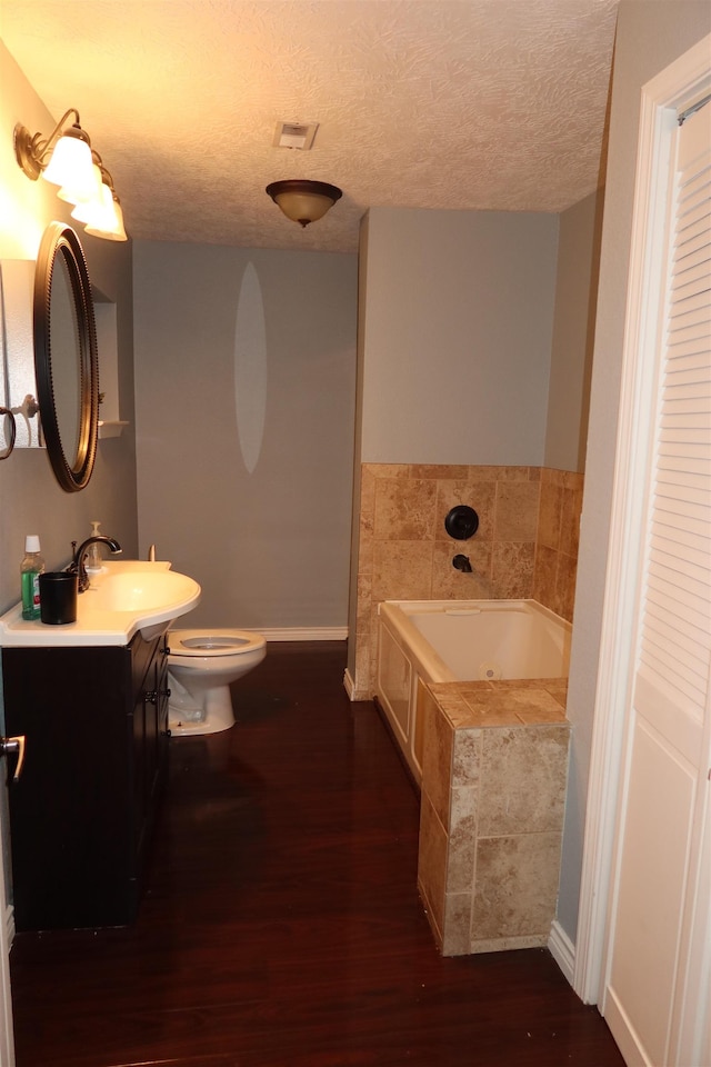 bathroom with vanity, hardwood / wood-style flooring, a relaxing tiled tub, toilet, and a textured ceiling