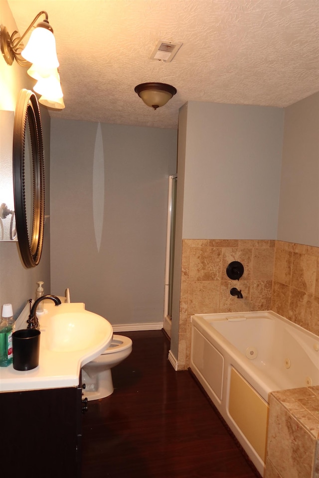 bathroom featuring wood-type flooring, a textured ceiling, a tub to relax in, and toilet