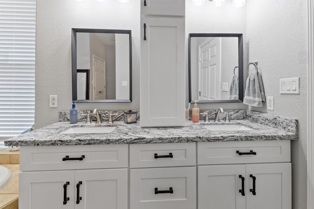 bathroom featuring a textured wall, double vanity, and a sink