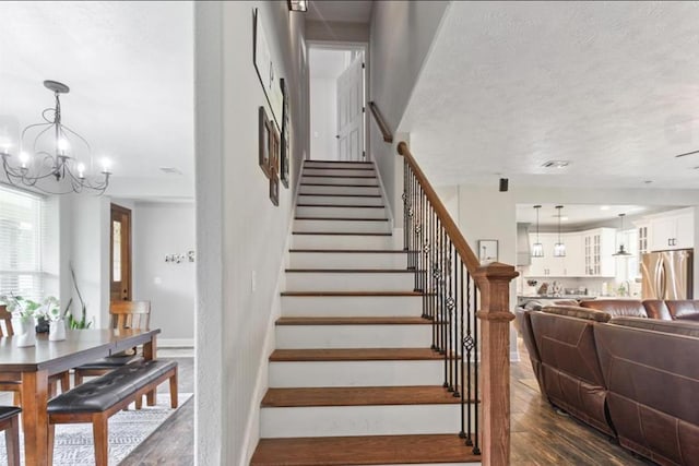 stairs with a chandelier, a textured ceiling, wood finished floors, and baseboards