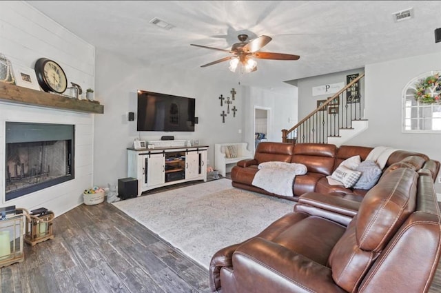 living room featuring a fireplace, visible vents, ceiling fan, wood finished floors, and stairs