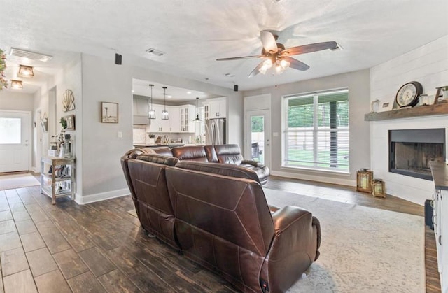 living area featuring dark wood-style floors, a fireplace, visible vents, and a ceiling fan