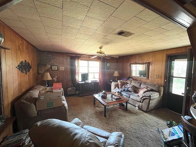 carpeted living area with visible vents, wood walls, and a ceiling fan