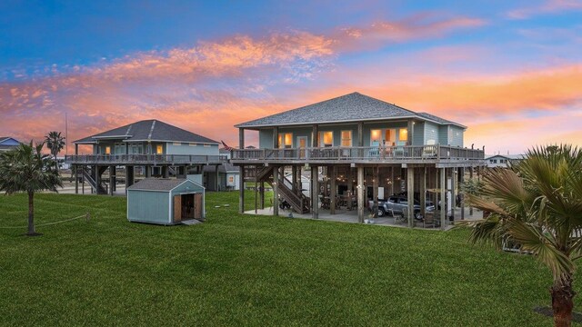 back house at dusk with a patio, a yard, and a storage unit