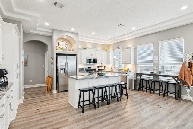 kitchen featuring a breakfast bar, a center island, stainless steel appliances, light stone countertops, and white cabinets