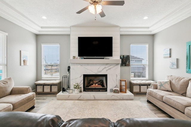 living room featuring ceiling fan, a textured ceiling, a fireplace, and light hardwood / wood-style floors