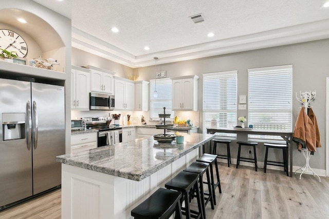 kitchen featuring a kitchen bar, white cabinetry, light stone counters, a center island, and stainless steel appliances