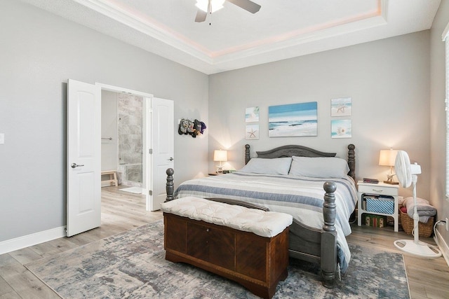 bedroom featuring a raised ceiling, ceiling fan, connected bathroom, and light wood-type flooring