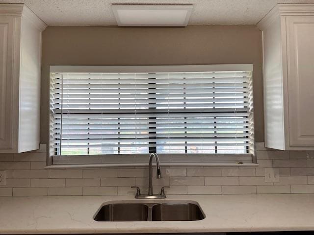 kitchen featuring tasteful backsplash, white cabinetry, sink, and light stone countertops