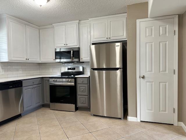 kitchen featuring appliances with stainless steel finishes, gray cabinets, white cabinetry, and light tile patterned flooring